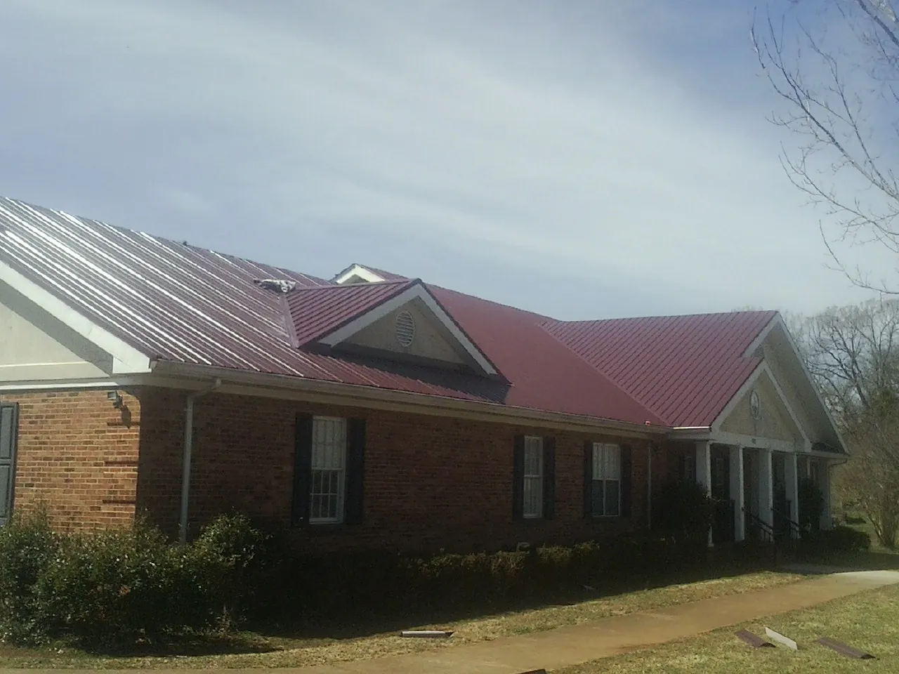 Red metal roof with gabled entries on a long brick building, from a Hail Damage Roof Repair job in Santa Rosa Beach