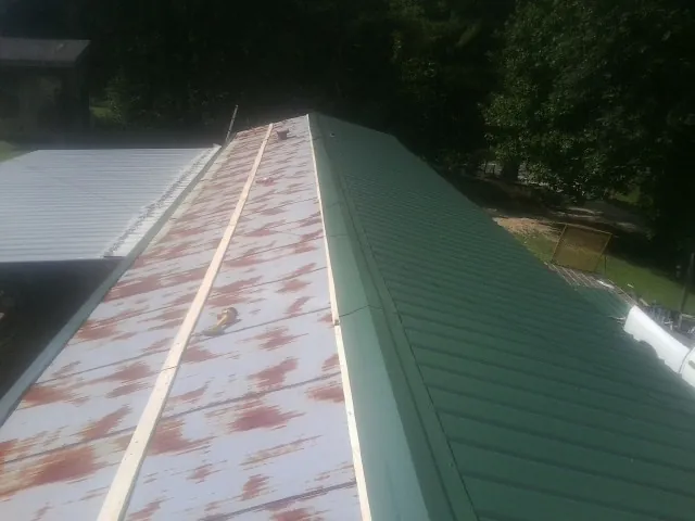 Old rusted panels beside newly installed green metal roofing — Wind Damage Roof Repair by Roofing Brothers in Santa Rosa Beach