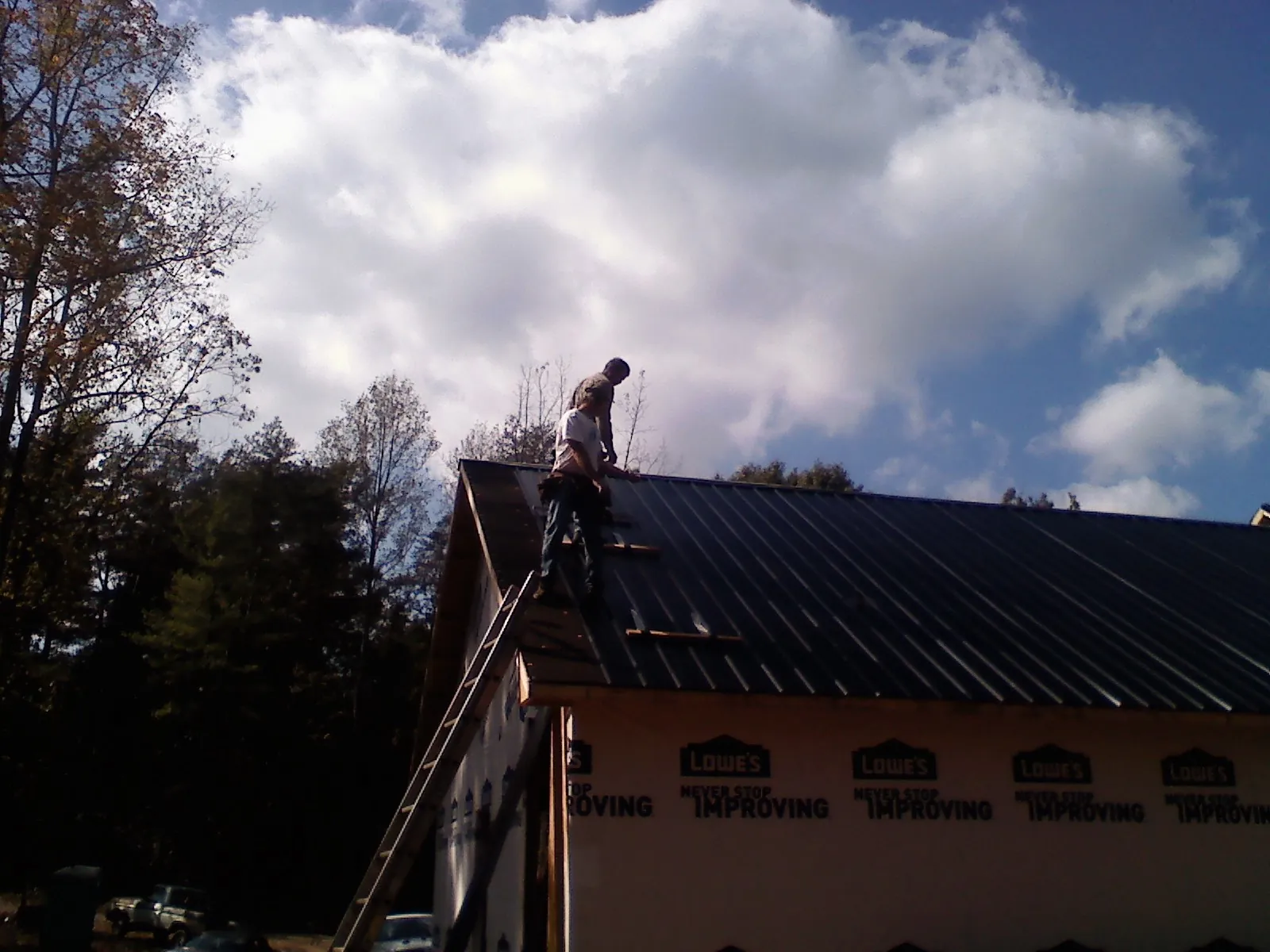 Roofer fastening dark metal panels high against a cloudy sky, from a Roof Inspection job in Santa Rosa Beach