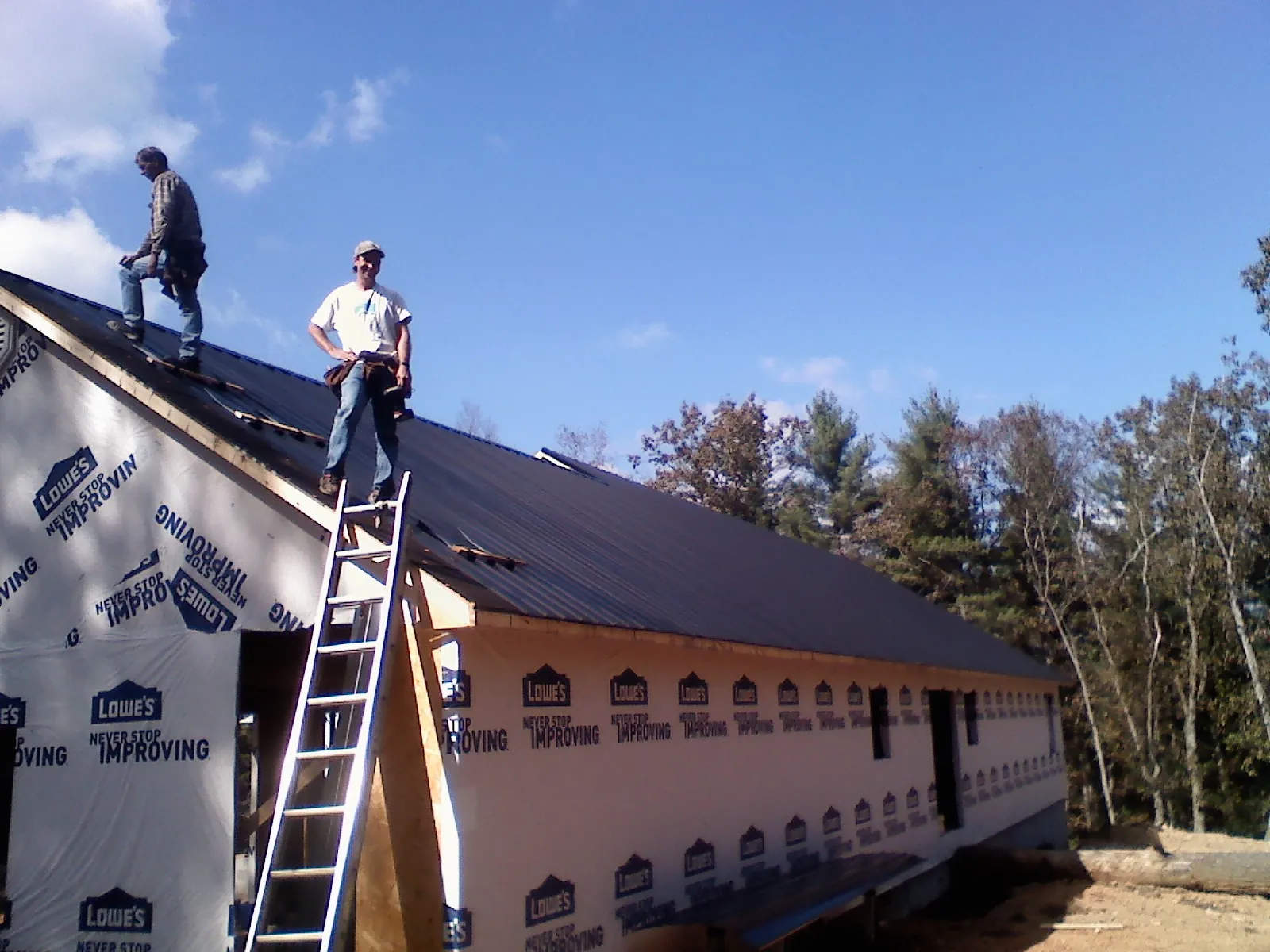 Two roofers standing on a long dark metal roof over a wrapped building in Santa Rosa Beach