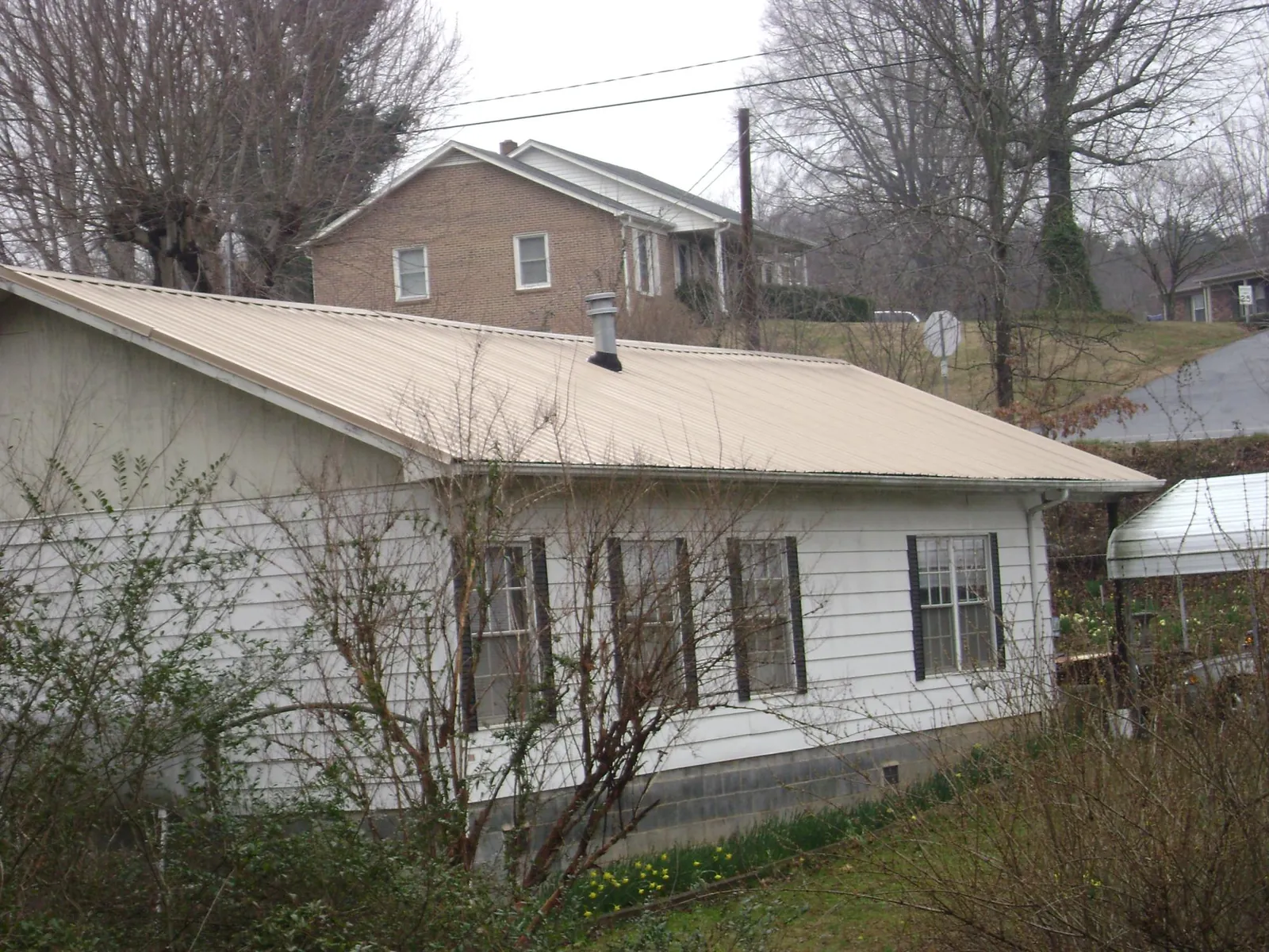 Tan metal roof on a white sided house set into a hillside — Commercial Roofing by Roofing Brothers in Santa Rosa Beach